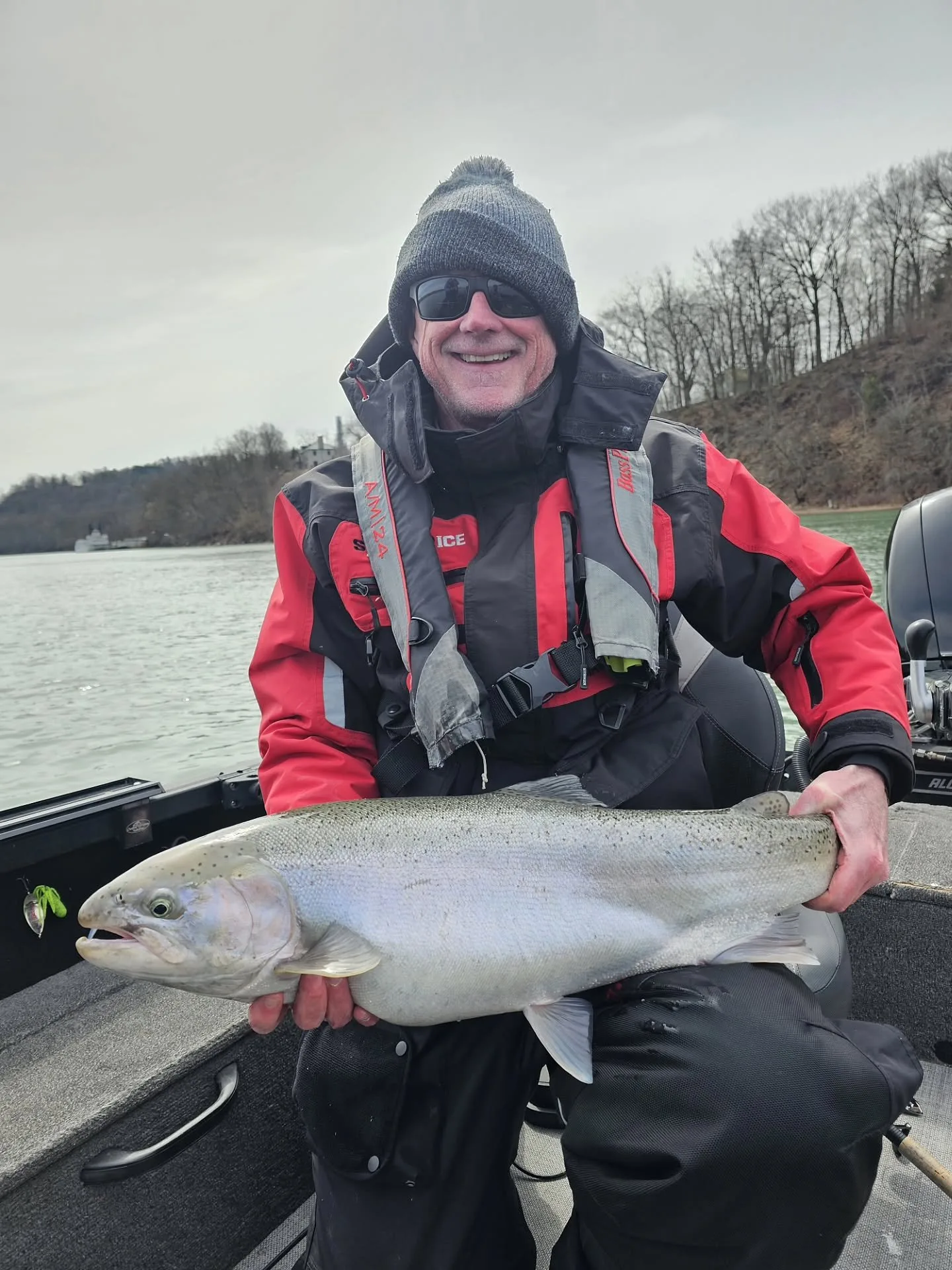 Angler in a red life jacket holding a steelhead below the river bluffs