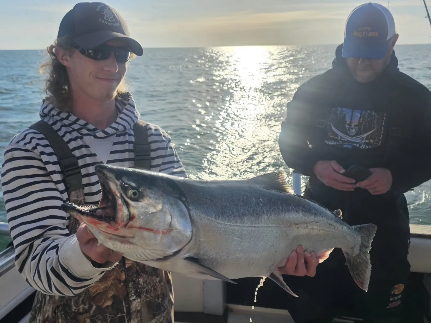 Angler holding a chinook salmon backlit by a sunset on the water