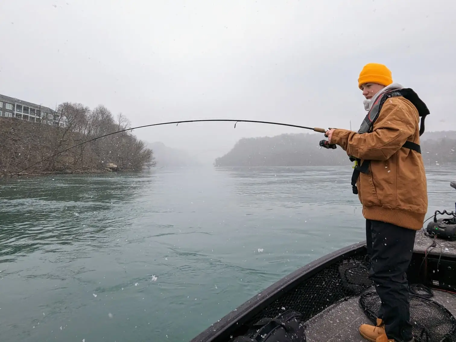 Angler fighting a fish on the Niagara River in falling snow, the gorge banks behind