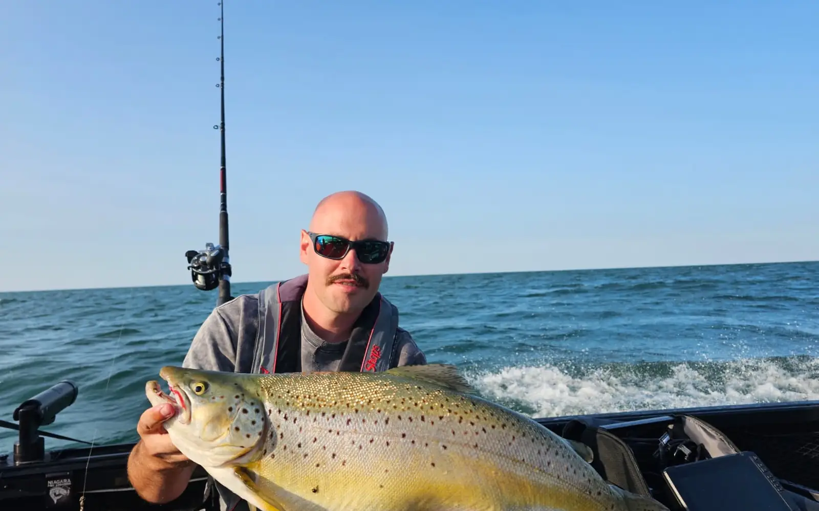 Angler holding a brown trout with the boat wake running out behind